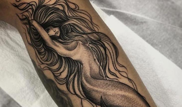 Imagem de tatuagem na panturrilha em preto e branco de uma sereia com cabelos esvoaçantes e sombreados pelo corpo trabalhados em pontilhismo