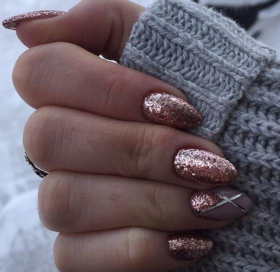 Mãos femininas mostram unhas feitas em material acrigel, de cor rosada e com glitter em todas as unhas. Uma das unhas tem desenhos geométricos