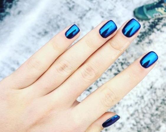 Mãos femininas mostram unhas feitas em material acrigel, da cor azul neon e brilhante.