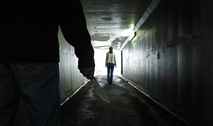 foto de uma pessoa em primeiro plano segurando uma faca, e outra à frente andando de costas para a primeira, ambos em um túnel