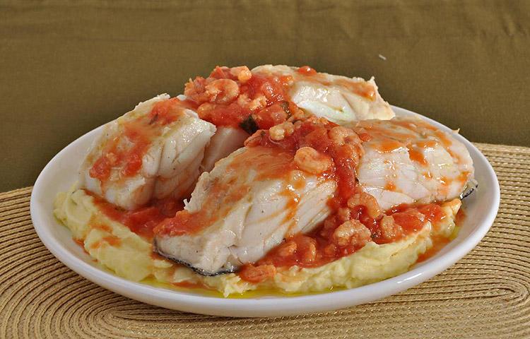 Bacalhau ao molho de camarão com purê em um prato branco redondo