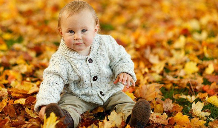 A foto mostra um bebê sentado em um monte de folhas laranjas, ilustrando uma das leis morais do espiritismo
