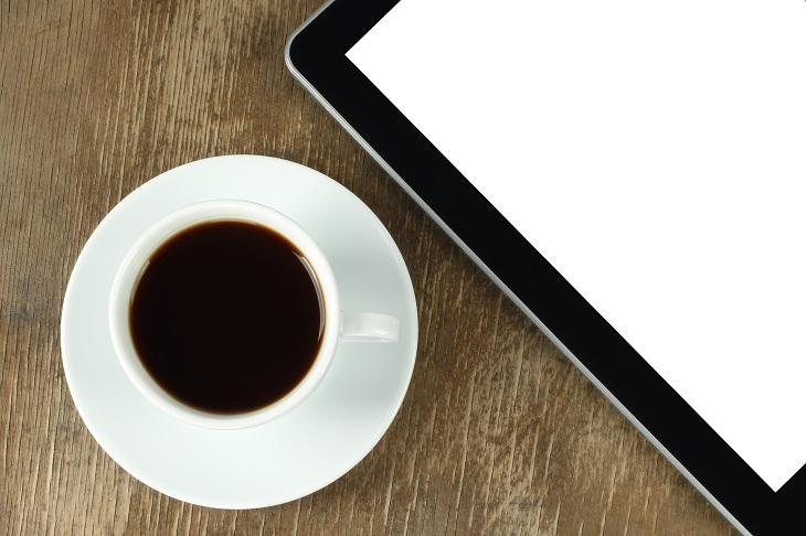 uma xícara de café e um tablet em cima de uma mesa de madeira