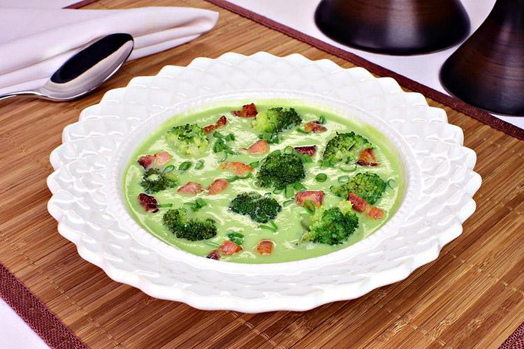 Caldo de brócolis com bacon em um prato redondo e decorado sobre uma mesa de madeira