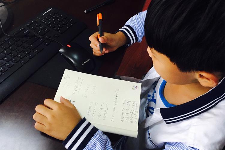 crianca escreve à mão em frente a um computador
