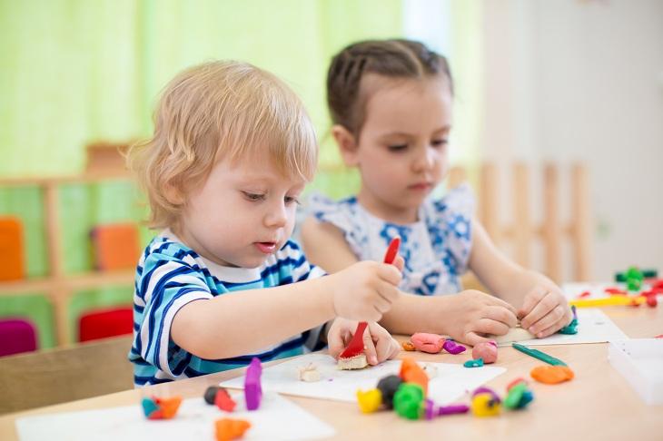 crianças sentadas em uma mesa brincando com massinhas coloridas