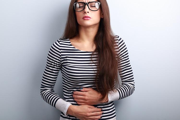 mulher de blusa listrada e óculos com as mãos nos estômago, expressão de dor de estômago