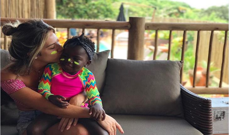 Giovanna Ewbank abraçando e beijando o rosto da filha Titi, ambas com protetor solar neon amarelo no rosto