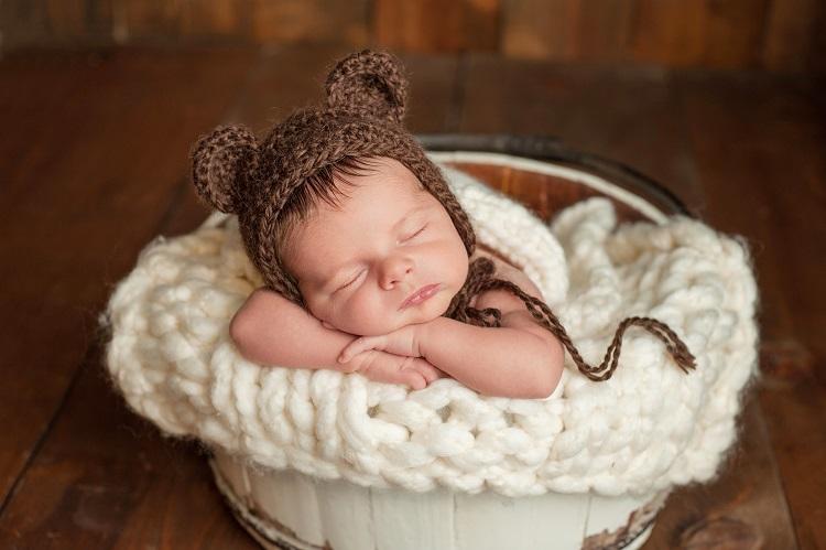 bebê dormindo em uma bacia com uma gorro de marro com orelhinhas de urso, acessório para ensaio newborn