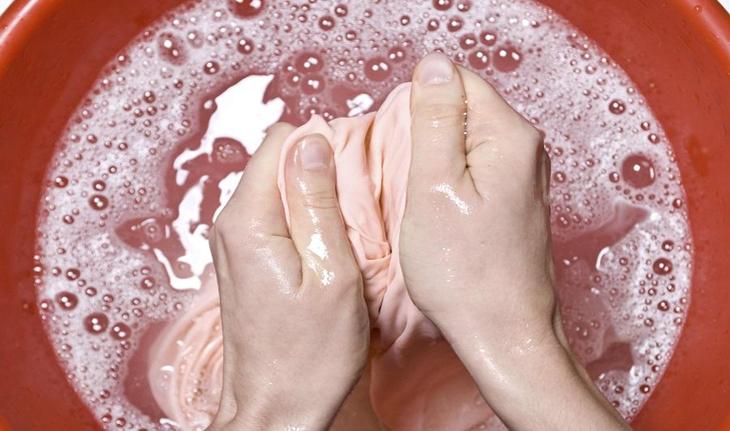 mãos lavando uma peça de roupa dentro de um balde vermelho