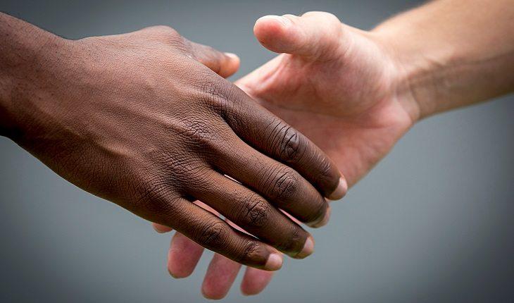 A foto mostra as mãos de uma pessoa negra e uma branca se cumprimentando, ilustrando uma das leis morais do espiritismo