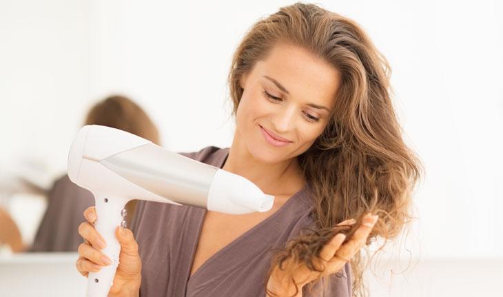 mulher com aparência feliz secando o cabelo com secador