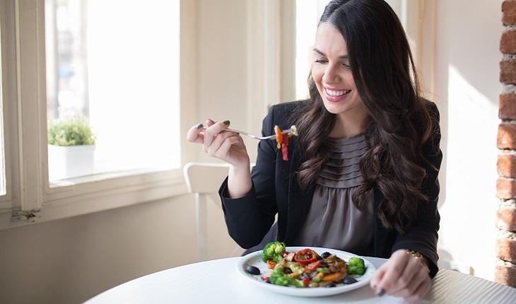 A foto mostra uma mulher comendo salada. Ela está de olhos fechados aproveitando a refeição. Essa é uma opção para começar a praticar a meditação mindfulness