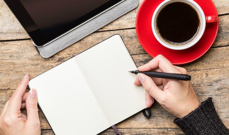 Caderno, mão de mulher, caneta, xícara de café e tablet