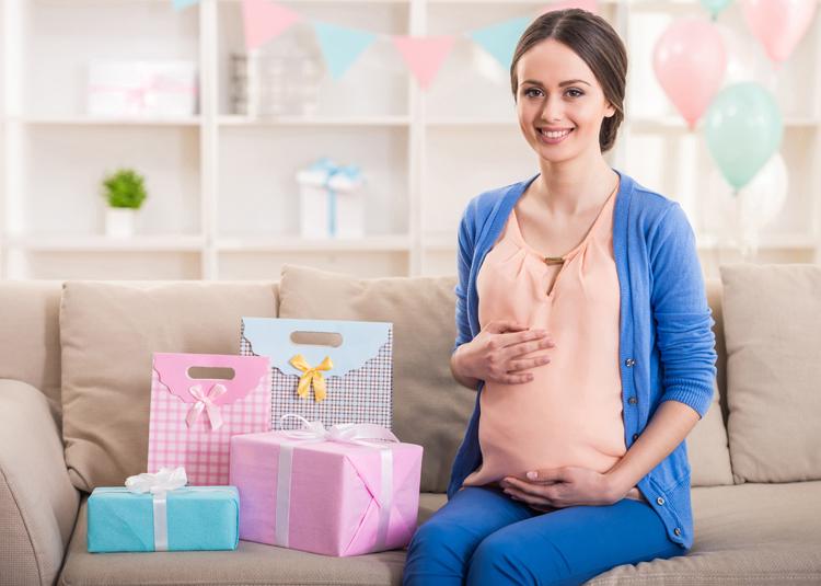 imagem de uma mulher grávida sentada em um sofá, sorrindo e ao lado de vários presentes