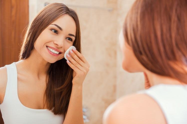 mulher em frente a um espelho limpando o rosto com uma esponjinha