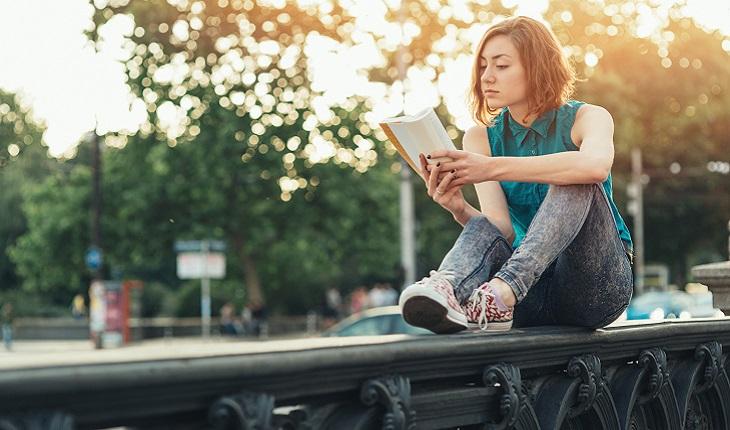 A foto mostra uma menina lendo sentada em uma grade na rua lendo para turbinar suas memórias
