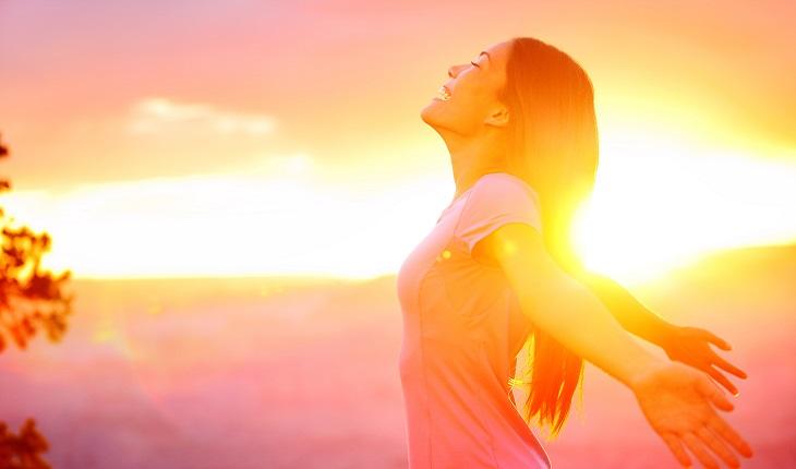 A foto mostra uma mulher ao ar livre sorrindo e recebendo a luz do sol na pele. Sentir o sol ajuda a focar e realizar a meditação mindfulness