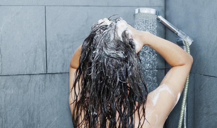 A imagem mostra uma mulher tomando lavando a cabeça no chuveiro. Se concentrar na percepção da água no banho é uma boa maneira de praticar a meditação mindfulness