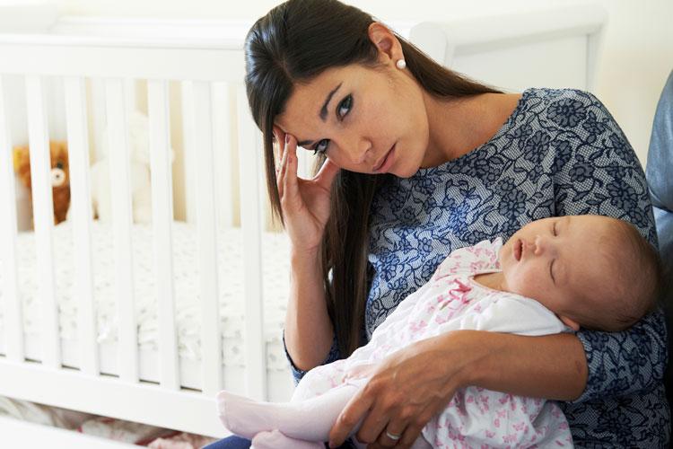 Mulher com cara de cansada segurando um bebê. Mulheres com filhos dormem menos
