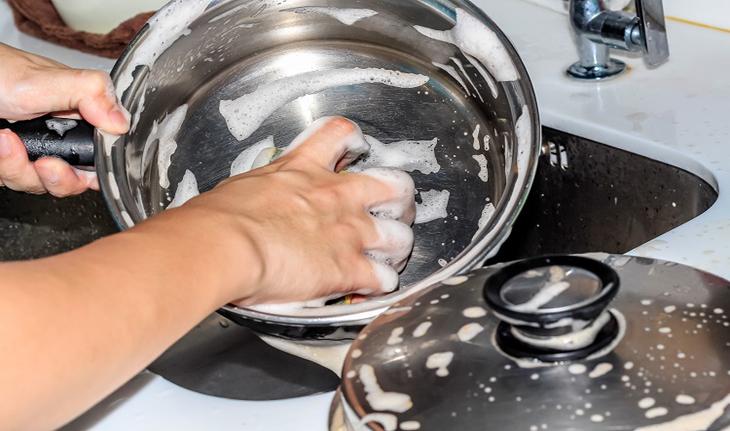 mão lavando panela de aço na pia