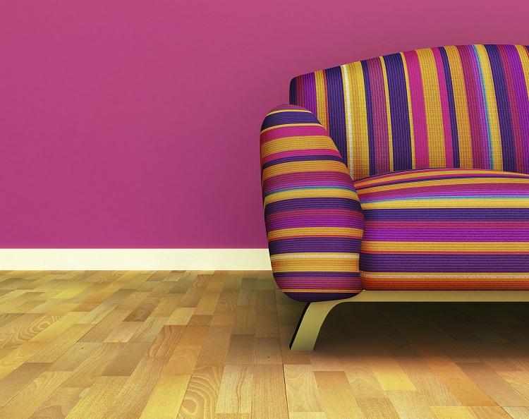 sofá listrado e colorido sobre um piso de madeira e com uma parede pink ao fundo