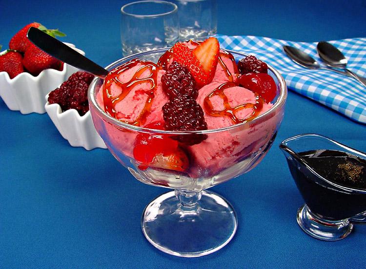 Sorvete de frutas vermelhas de coloração rosa em uma taça de sobremesa com frutas vermelhas em cima