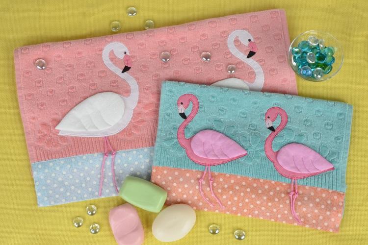 duas toalhas, de rosto cor-de-rosa e de lavabo azul. ambas com patch apliquê de flamingos, fundo amarelo sabonetes ao redor