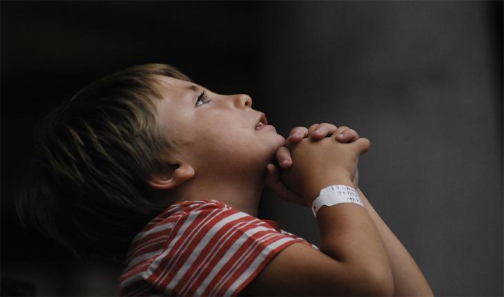Menino de cor branca olhando para cima com as mãos juntas em sinal de oração. Provérbios