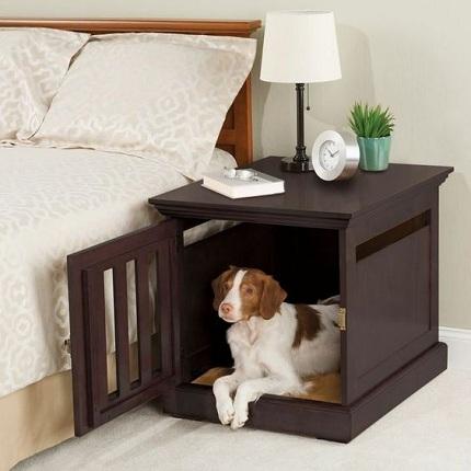 Foto de uma casinha de cachorro feita dentro de um criado-mudo localizado ao lado de uma cama de casal