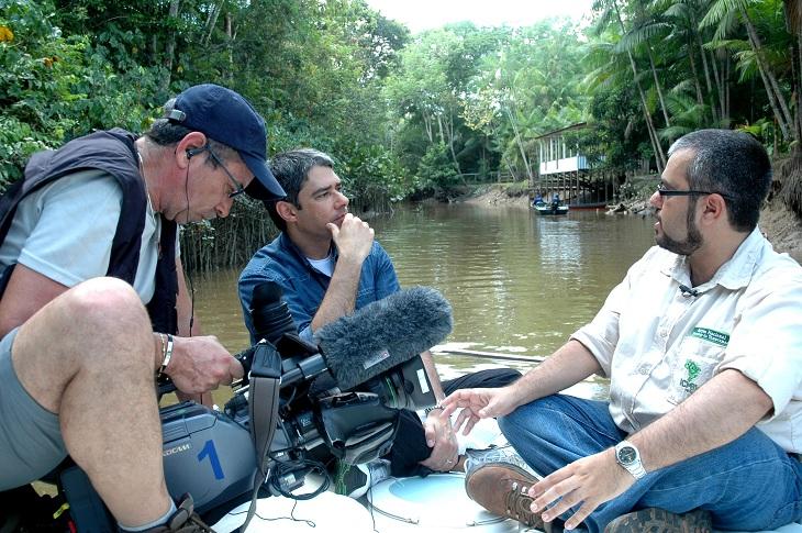 William Bonner e um homem com uma câmera em cima de um barco realizando uma entrevista com um terceiro homem, à direita