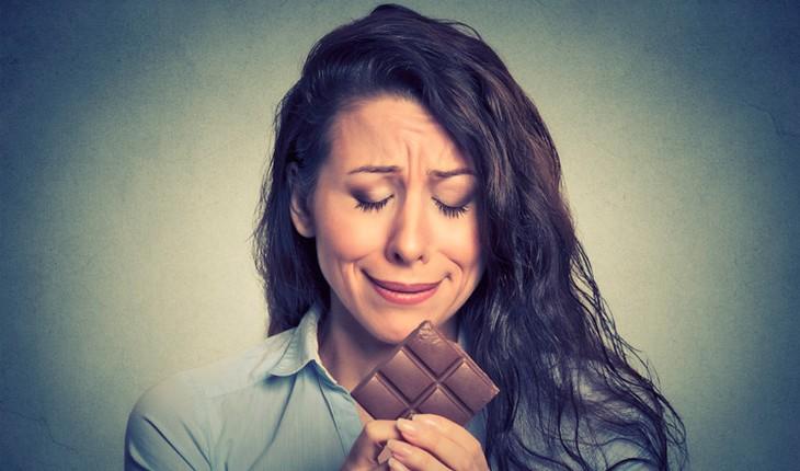 mulher olhando para uma barra de chocolate com cara de tristeza