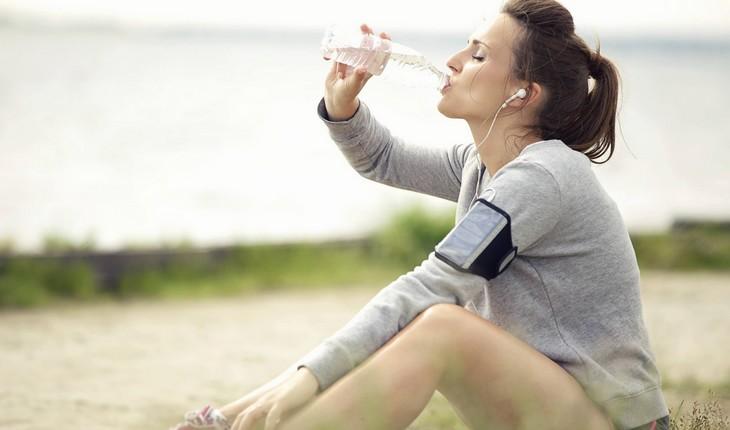 mulher sentada bebendo água com trajes de corrida