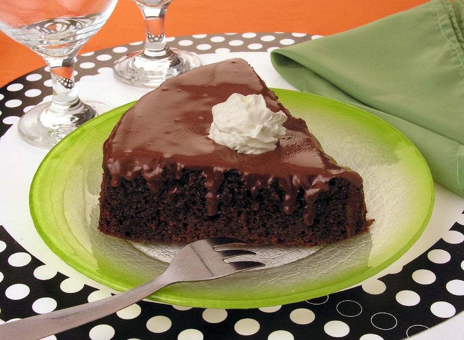 O pedaço do bolo de chocolate com calda de ameixa está sobre um prato verde redondo e está decorado com um pouco de chantilly na parte de cima