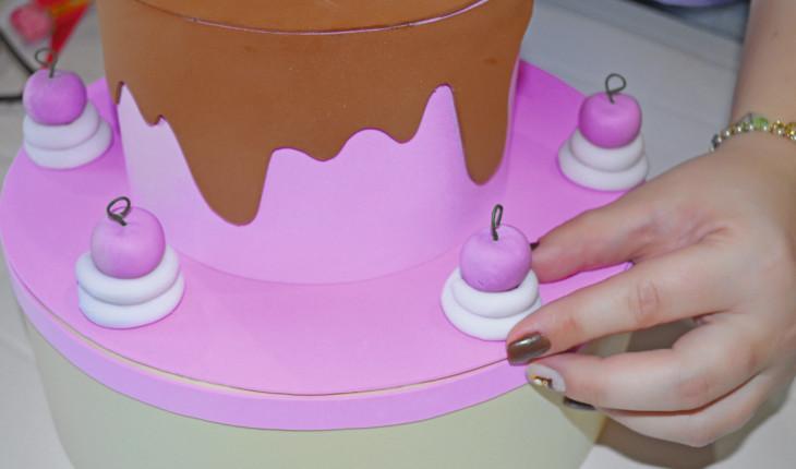 Na foto é possível ver as pessoas colando as cerejinhas reservadas ao redor do bolo do topo, na parte de cima do bolo intermediário.