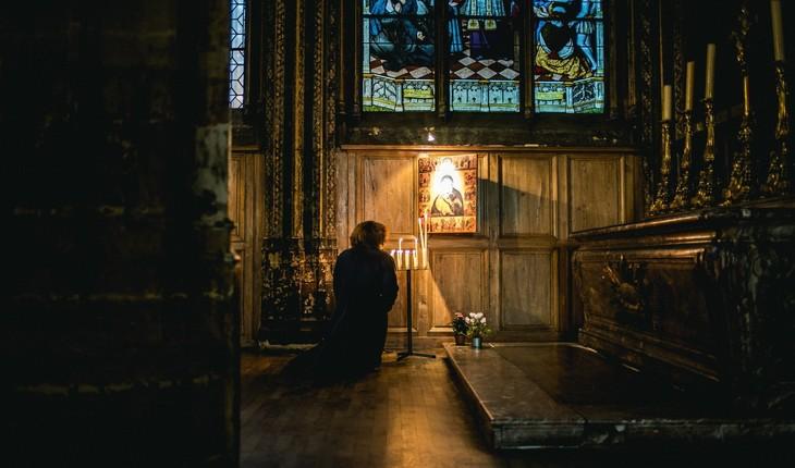Mulher em igreja escura, iluminado apenas o altar, rezando. Provérbios