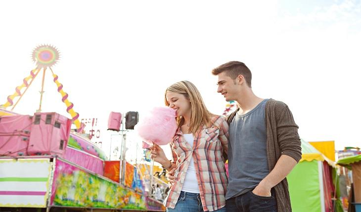 Casal de namorados andando por um parque de diversões, moça segurando um algodão doce