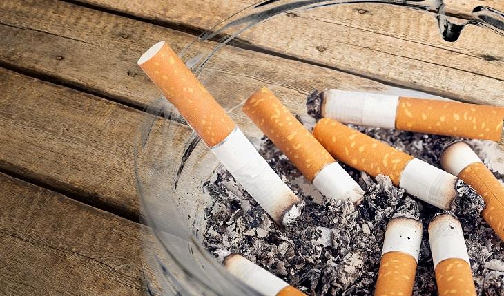 A foto mostra um cinzeiro com bitucas de cigarro.