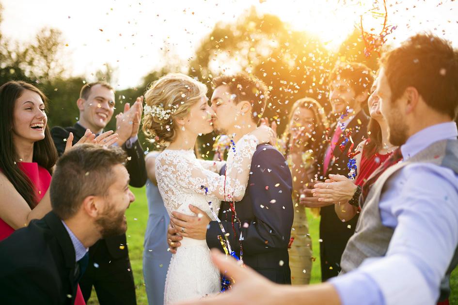 Noivos se beijando em um casamento durante o dia com comemoração de amigos