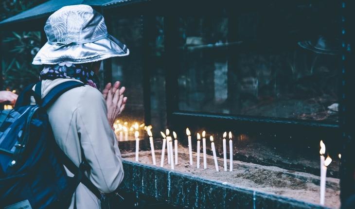 Mulher branca de costas em frente a altar com velas rezando. provérbios