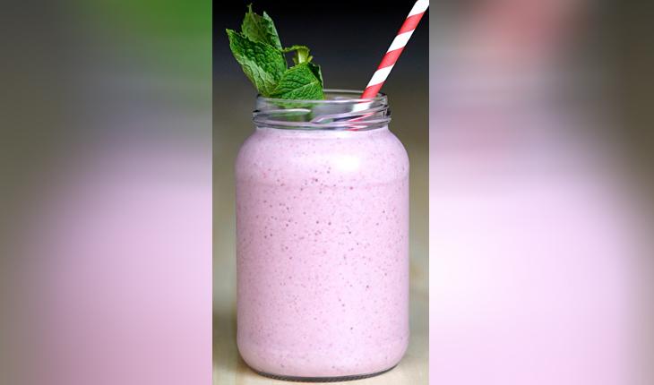 pote de vidro transparente, cheio com iogurte rosa e decorado com um ramo de hortelã e um canudo listrado branco e vermelho
