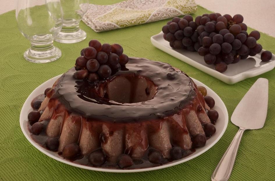 O manjar de vinho está sobre uma prato branco redondo e há um cacho de uva por cima para decorar