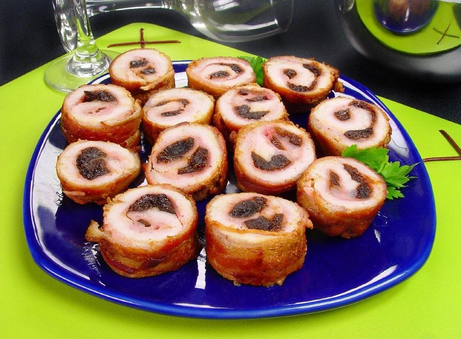 O medalhão de lombo com bacon está em um prato redondo azul e há várias unidades. É possível ver as ameixas que recheiam os pedaços. 