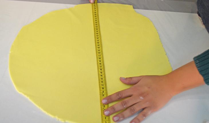 Na foto há uma pessoa utilizando uma fita métrica para medir a quantidade de pasta americana