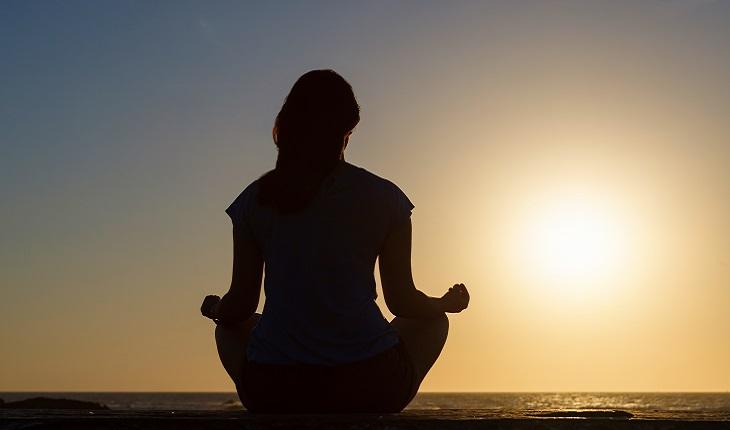 A foto mostra a silueta de uma mulher sentada praticando mindfulness ao nascer do sol