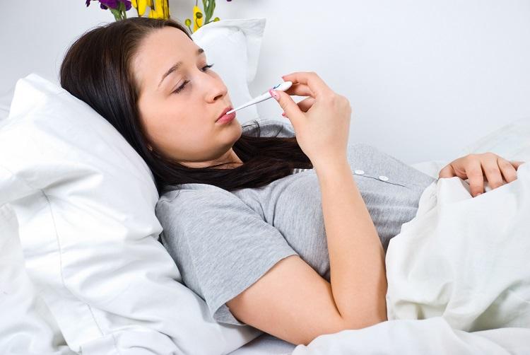 mulher deitada na cama, doente, com termômetro na boca.