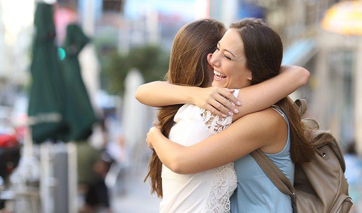 A foto mostra duas amigas se abraçando e sorrindo