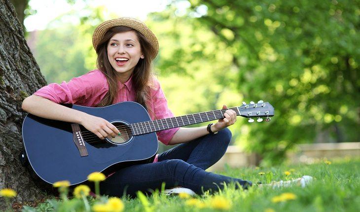 foto de uma mulher sentada embaixo de uma árvore, tocando violão