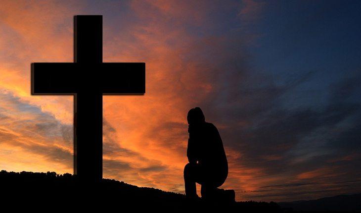 pessoa rezando em frente à uma cruz