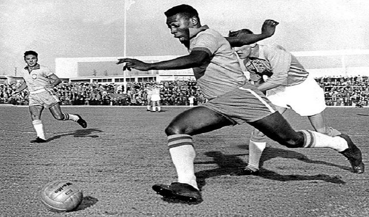 Pelé jogando futebol no estádio usando a camiseta da seleção brasileira e correndo do zagueiro
